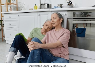 An older lesbian couple takes a break from cleaning their modern kitchen, leaning against the cabinets. - Powered by Shutterstock