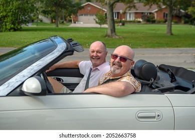 Older Male LGBT Gay Couple Enjoying  A Sunny Day And Driving In Their White Convertible With The Top Down.  The Couple Is Smiling And Happy.