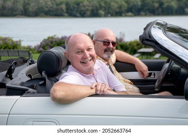 Older Male LGBT Gay Couple Enjoying  A Sunny Day And Driving In Their White Convertible With The Top Down.  The Couple Is Smiling And Happy.