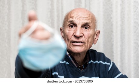 Older Male Patient Holds Facemask In Hand And Shows It With Resentment. Lockdown And Quarantine Concept.