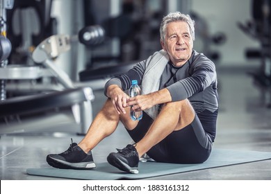 Older Male Rests With A Bottle Of Water Sitting On A Mat During A Gym Workout.