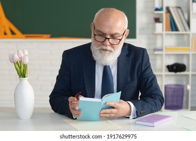 Older Male Teacher Standing In Front Of A Chalkboard In A Classroom