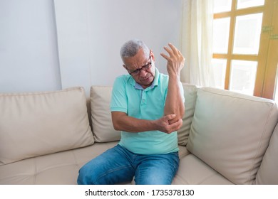 Older Man With Arm Pain Sitting On His Couch At Home, Feels Sick