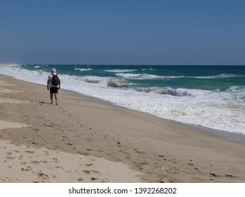 Older man with black backpack goes barefoot along the long, lonely sandy beach - Powered by Shutterstock