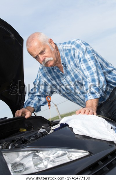 older man\
checking levels and servicing his\
car
