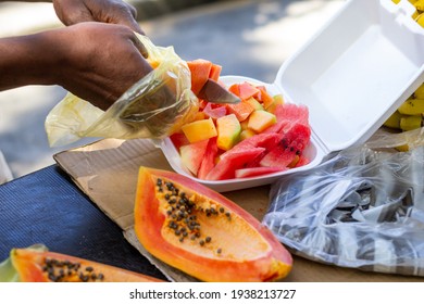 Older Man Cutting Fresh Fruit Into A Plastic Container For A Customer Together With A Papaya Cut In Half