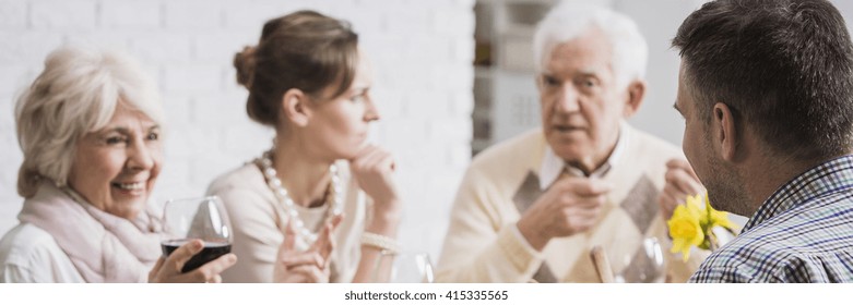 Older Man Discussing With His Adult Kids During Family Supper. Older Smiling Mother Drinking Red Wine