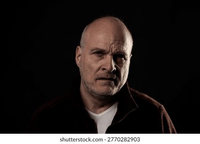Older man expressing deep thought and seriousness on a black background, facing the viewer