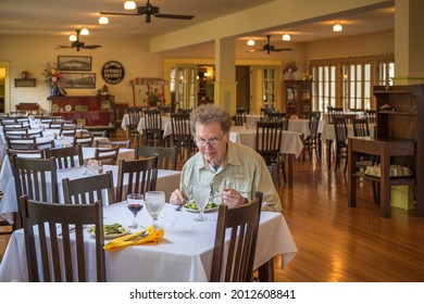 Older Man In Eye Glasses Eating Dinner In Large Dining Room Of Midwestern Resort; Man Looking At Camera; Tables And Chairs In Background