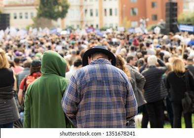 An older man faces down while in front of a crowd which gives a small feeling of sadness.