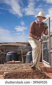 Older Man Gardening With Pitchfork In Garden Bed