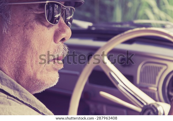 Older man with glasses\
driving a car