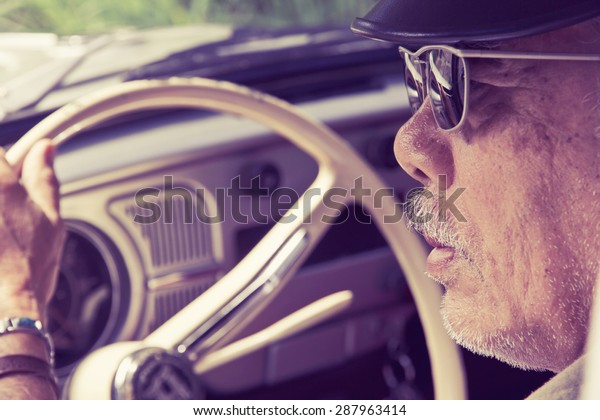 Older man with glasses\
driving a car