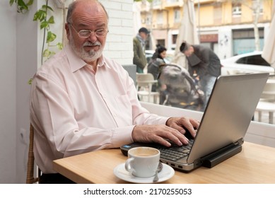 An Older Man With Glasses Sitting In A Coffee Shop With His Laptop Makes A Funny Face