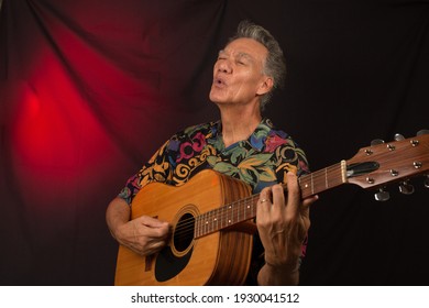 Older Man Having Fun Playing His Acoustic Guitar Against A Red Lit Background