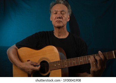 Older Man Having Fun Playing His Acoustic Guitar Against A Blue Lit Background