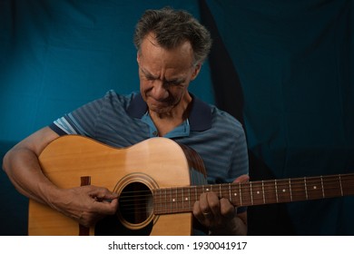 Older Man Having Fun Playing His Acoustic Guitar Against A Blue Lit Background