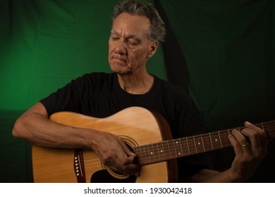 Older Man Having Fun Playing His Acoustic Guitar Against A Green Lit Background