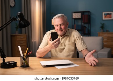 Older Man Laughs Into His Phone Webcam. Elderly Executive Is Video Conferencing On His Phone. Senior Man Is Chatting Online. The Grey-haired Man Is Gesturing With His Hands While Talking On The Phone