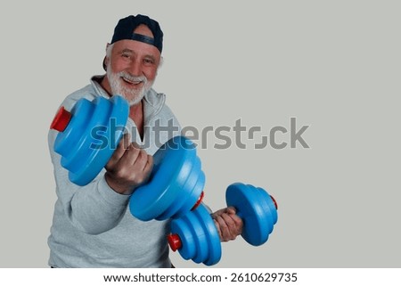 An older man laughs while training with blue dumbbells. Strong and active, he lives his motto, Staying fit with age. Joy and movement go hand in hand.