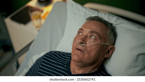 Older man lies in a hospital bed with an oxygen tube in his nose, taking a moment to rest and recover. - Powered by Shutterstock