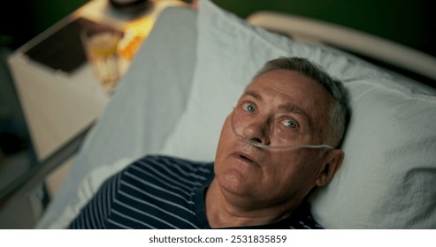 Older man lies in a hospital bed with an oxygen tube in his nose, taking a moment to rest and recover. - Powered by Shutterstock