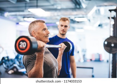 Older man lifting weights, supervised by gym assistant. Sporty lifestyle of elderly people. - Powered by Shutterstock