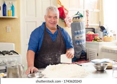 Older Man Making Bread At Home - Hispanic Man Preparing Dough For Bread- Smiling Grandfather Baking Looking At Camera