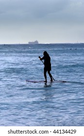 Older Man Paddle Boards Across Waikiki Bay While Ship Is Leaving Port.  Evening Light Silhouettes Paddler.