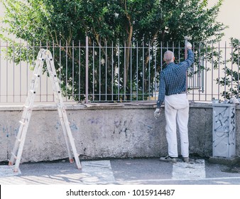 Older Man Painting A Fence With Ladder