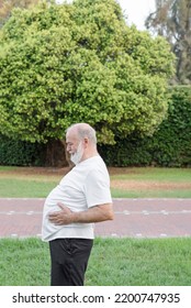 An Older Man In The Park Touches His Big Belly With His Hands Before Practicing Sport To Lose Weight