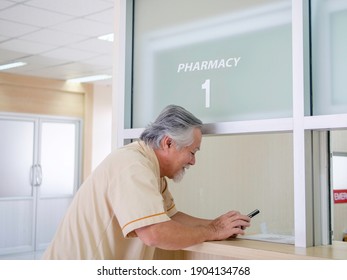 Older Man Patient Using The Mobile Banking Application To Paying Exam. Asian Elderly Man Standing In The Front Of  Cashier Counter In Hospital. For Paying Bill Through Smartphone Concept.