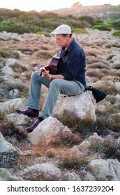 Older Man Playing Guitar In Full Rocky Landscape Of Menorca