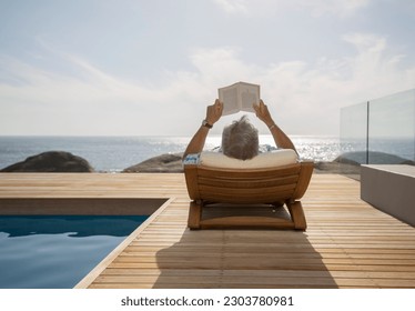 Older man reading by pool - Powered by Shutterstock