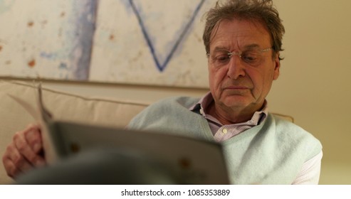 Older Man Reading Magazine While Seated On Living Room Sofa