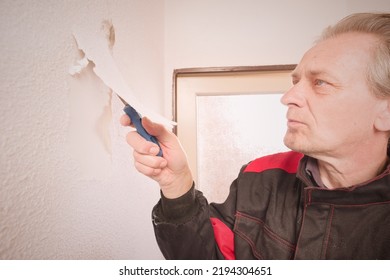 Older Man Removing Old Wallpapers Off The Walls In Empty Apartment