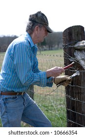 Older Man Repairing A  Broken Fence With A Hammer And Fence Pliers