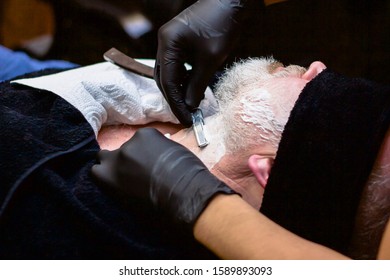 An Older Man Is Shaved In A Barber Shop. A Professional Worker Applies Shaving Foam To The Face Of A Client. Beauty And Care For Your Appearance Handsome Beauty And Care For Your Appearance