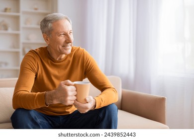 An older man sits comfortably on a couch, holding a warm cup, signifying relaxation or a coffee break - Powered by Shutterstock