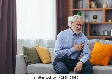 The older man sits at home alone, the grandfather holds his hands on his chest, his heart aches - Powered by Shutterstock