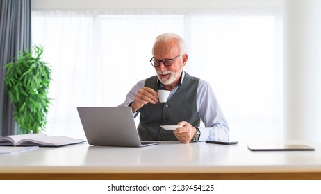 Older man sitting at the desk in his office drinking coffee or espresso reading business reports and looking satisfied and happy - Powered by Shutterstock