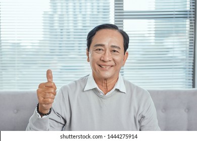 Older Man Sitting On Couch Giving Thumb Up While Playing Computer Game, Looking At Camera, Smiling.?