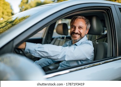 An Older Man Smiling In The Camera While He Prepares To Drive A Car.