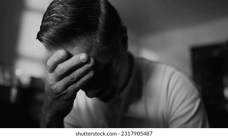 Older man struggling with trauma and loneliness. Middle-aged male person covering face looking down in shame and despair. Hopeless feeling depicted in monochrome black and white - Shutterstock ID 2317905487