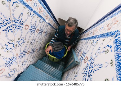 Older Man Taking Clothes Up To The Terrace Up The Stairs To Hang Them After Doing The Laundry. Homework. Househusband. Selective Focus.