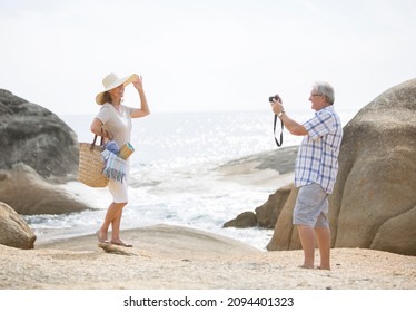 Older Man Taking Pictures Of Girlfriend On Beach