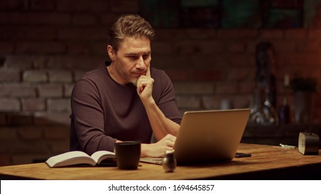 Older man tele working with laptop computer at home office in dark room, thinking, looking busy. - Shutterstock ID 1694645857
