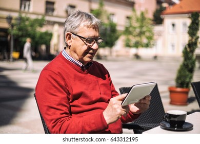 Older Man Using Digital Tablet While Drinking Coffee At The Bar.Senior Man With Digital Tablet
Image Is Intentionally Toned.