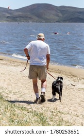 Older Man Walking His Dog On Leash On A Beach