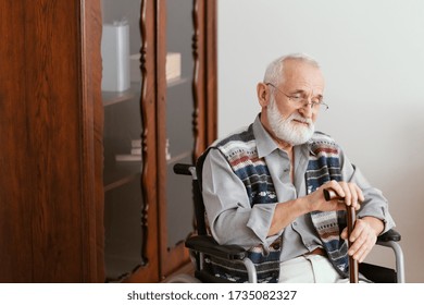 Older man with a walking stick sitting on a wheelchair home alone